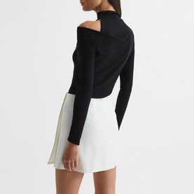 Model wearing Reiss Amy Cut Out Shoulder Top in black, high neck, asymmetric cut-out shoulder, long sleeves, styled with white mini skirt