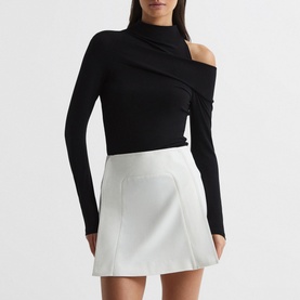 Model wearing Reiss Amy Cut Out Shoulder Top in black with asymmetric neckline, styled with a white mini skirt