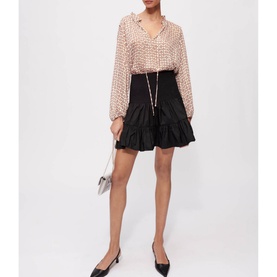 Model wearing Maje Jun Smock Ruffle Mini Skirt in black with elasticated waist, styled with a printed blouse and black flats