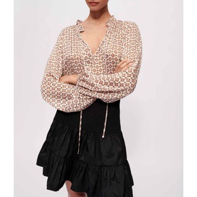 Model wearing Maje Jun Smock Ruffle Mini Skirt in black, styled with a geometric print long-sleeve blouse with tie detail