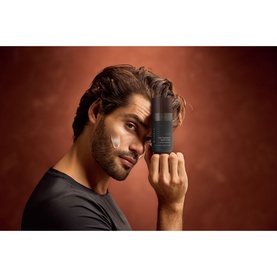 Model with Rituals Homme 24h Hydrating Face Cream pump bottle held to face, wearing dark t-shirt, terracotta background