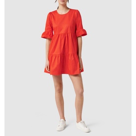 Model wearing Forever New Matilda Cotton Smock Dress in red, featuring frill cuffs, tiered skirt, and round neck, styled with white trainers