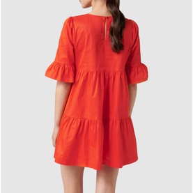 Model wearing Forever New Matilda Cotton Smock Dress in red-orange, showing tiered skirt, frill cuffs, and button back fastening