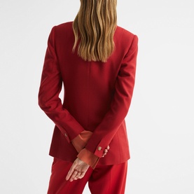 Model wearing Reiss Lola Double Breasted Blazer in red, back view showing vent detail and gold button cuffs, styled with matching red trousers