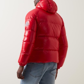 Model wearing Pyrenex Sten Puffer Jacket in red, rear view, showing logo patch, padded design and adjustable hood, styled with blue jeans