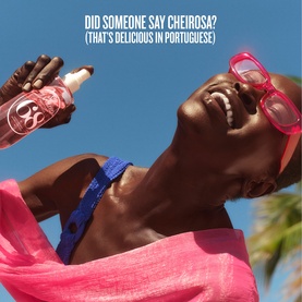Model with Sol De Janeiro Brazilian Crush Cheirosa 68 Body Mist, wearing pink sunglasses and bikini top, laughing outdoors