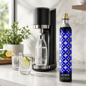 SodaStream sparkling water maker in black with chrome detail, styled with CO₂ cylinder, glass bottle, and two drinks with lime on white marble surface