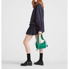 Model carrying Prada Re-Edition 2005 Saffiano Leather Bag in green with chain handle, styled with navy sweatshirt, pleated mini skirt and black boots