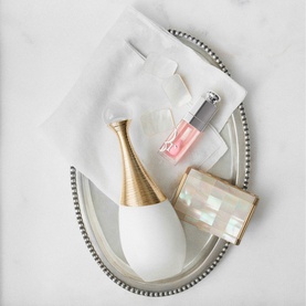 Dior J'adore Parfum d'Eau EDP in white and gold bottle, styled on silver tray with pink nail polish and face mask