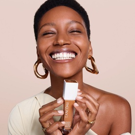 Model with Lanc&ocirc;me Teint Idole Ultra Wear Care & Glow Foundation 30ml, wearing gold hoop earrings and rings, smiling broadly