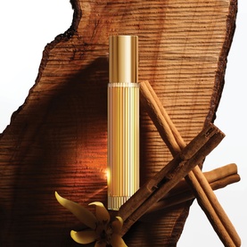 Gold ribbed fragrance rollerball displayed with cinnamon sticks and warm candlelight against a wood slice backdrop