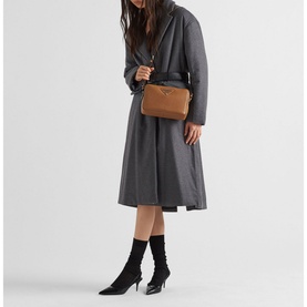 Model carrying Prada Accessories Leather Shoulder Strap Bag in brown with gold hardware, styled with grey coat and black heeled boots