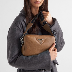 Model carrying Prada Accessories Leather Shoulder Strap Bag in brown, silver-tone hardware, woven tape and leather straps, double zip closure
