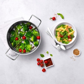 Zwilling Plus Steamer Insert 24cm in silver satin finish, shown steaming broccoli and tomatoes, styled with a pasta dish alongside