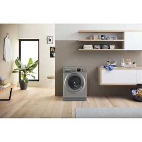 Hotpoint 8kg Freestanding Washing Machine in graphite, shown in a styled laundry room with wooden shelving and plant d&eacute;cor