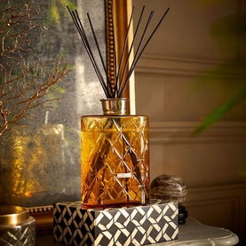 Rituals Oval Bottle Cognac gold reed diffuser with diamond-cut amber glass and black reeds, styled on decorative books in warm ambient setting