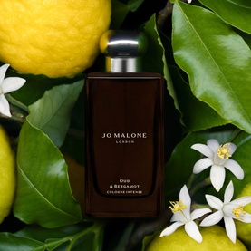 Jo Malone Oud & Bergamot Cologne Intense dark glass bottle surrounded by fresh lemons, green leaves and white blossom flowers