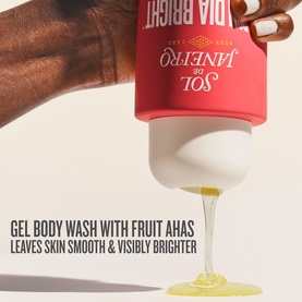 Sol De Janeiro Bom Dia Bright Body Wash being squeezed, releasing golden gel formula with foamy lather onto a glass surface