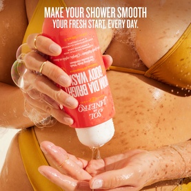 Model with Sol De Janeiro Bom Dia Bright Body Wash, dispensing product into palm, wearing yellow bikini top