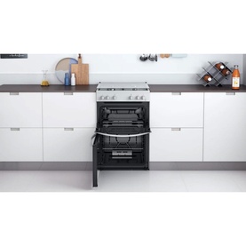 Indesit white 60cm freestanding gas double cooker with both oven doors open, shown in a modern white kitchen setting