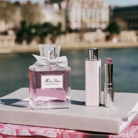 Dior Miss Dior Blooming Bouquet Eau de Toilette styled with a pink lipstick and lip gloss on a marble surface by a river.