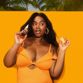 Model with Sol De Janeiro Brazilian Crush Cheirosa 62 Perfume Mist, holding bottle and lemon, wearing orange swimsuit