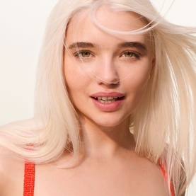 Model with glowing skin and platinum blonde hair, styled in Sol De Janeiro Brazilian Joia Strengthening + Smoothing Shampoo campaign shot