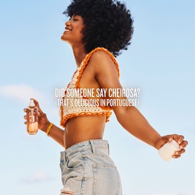 Model with Sol De Janeiro Brazilian Crush Cheirosa 71 Perfume Mist, holding bottle aloft, wearing orange crochet top and denim jeans