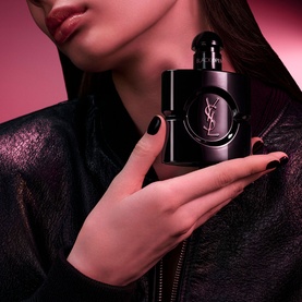 Model with YSL Black Opium Le Parfum, holding the sleek black bottle with gold YSL logo, wearing a black jacket with dark red lips.