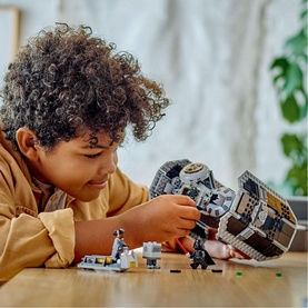 Child building the LEGO Star Wars TIE Bomber set on a table, with minifigures visible alongside the partially assembled grey model