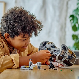 Child building Lego Star Wars TIE Bomber set, 625-piece multicoloured construction toy, with minifigures on table