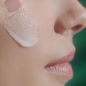 Model with Sisley Ecological Compound serum applied to cheek, showing smooth white fluid texture on skin