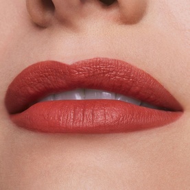 Model wearing Est&eacute;e Lauder Pure Color Matte Lipstick in Next Romance, a warm terracotta-red matte shade, shown as a close-up lip shot