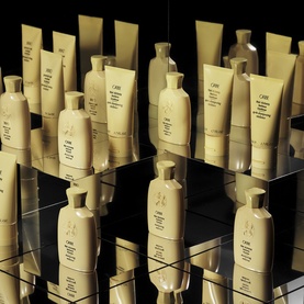Oribe Hair Alchemy Shampoo Travel 75ml displayed among full collection of gold hair care bottles and tubes on mirrored surface
