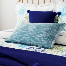 Helena Springfield Pom Pom Cushion in dark blue velvet with navy pom pom trim, styled on a bed with floral bedding and teal cushion