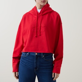 Model wearing Ganni Isoli Oversized Cropped Hoodie in red with tonal logo detail, styled with blue denim jeans