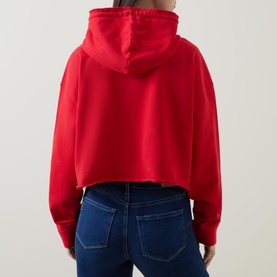 Model wearing Ganni Isoli Oversized Cropped Sweatshirt in red, back view, with dark blue jeans. Hooded with rolled hem