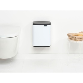 Brabantia Bo Waste Bin 7L in White with dark grey lid, mounted on wall in bathroom setting beside toilet and storage basket