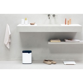 Brabantia Bo Waste Bin 7L in White with navy lid, placed on bathroom floor beside a minimalist sink and sandals