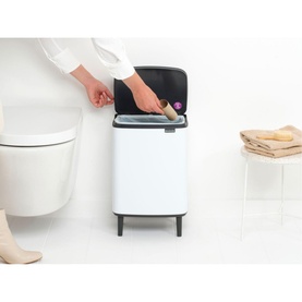 Brabantia Bo Waste Bin Hi 12L in White, shown in bathroom setting with hand depositing item, toilet and folded towels visible