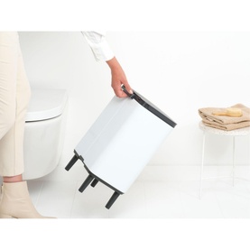 Brabantia Bo Waste Bin Hi 12L in White, shown being lifted by transport grip handle, with toilet and towels visible in bathroom setting