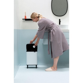 Model wearing grey robe using Brabantia Bo Waste Bin Hi 12L in white, opening lid in a modern bathroom setting