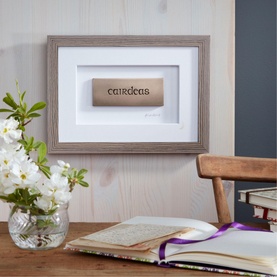 Wild Goose Cairdeas Picture, bronze cold cast resin word plaque in warm grey wooden frame, styled on desk with flowers and open journal