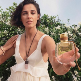 Model with Chlo&eacute; Nomade Jasmin Naturel Intense Eau de Parfum 75ml, holding bottle toward camera, wearing white dress and pendant necklace