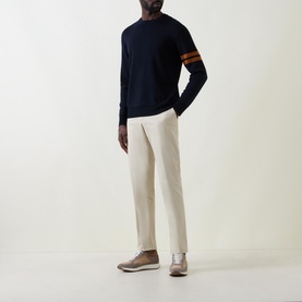 Model wearing Zegna Wool Stripe Sleeve Sweater in navy with orange stripe detail, styled with cream trousers and silver shoes