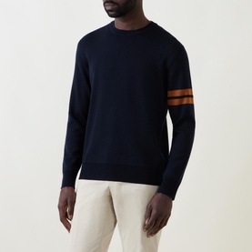 Model wearing Zegna Wool Stripe Sleeve Sweater in navy with camel stripe sleeves, crew neck and ribbed trims, styled with cream trousers