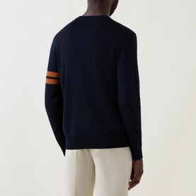 Model wearing Zegna Wool Stripe Sleeve Sweater in navy, showing rear view with tan stripe detail on sleeve, styled with cream trousers