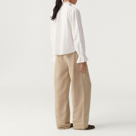 Model wearing Bash Feely Shirt in cream with embroidered detail and frill cuffs, styled with wide-leg beige trousers. Rear view