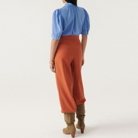 Model wearing Bash Tyler Top in blue cotton with balloon sleeves and pintuck pleats, styled with rust wide-leg trousers and tan boots