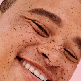 Close-up of smiling model with freckled skin showcasing natural brows, styled with Benefit Goof Proof Brow Powder